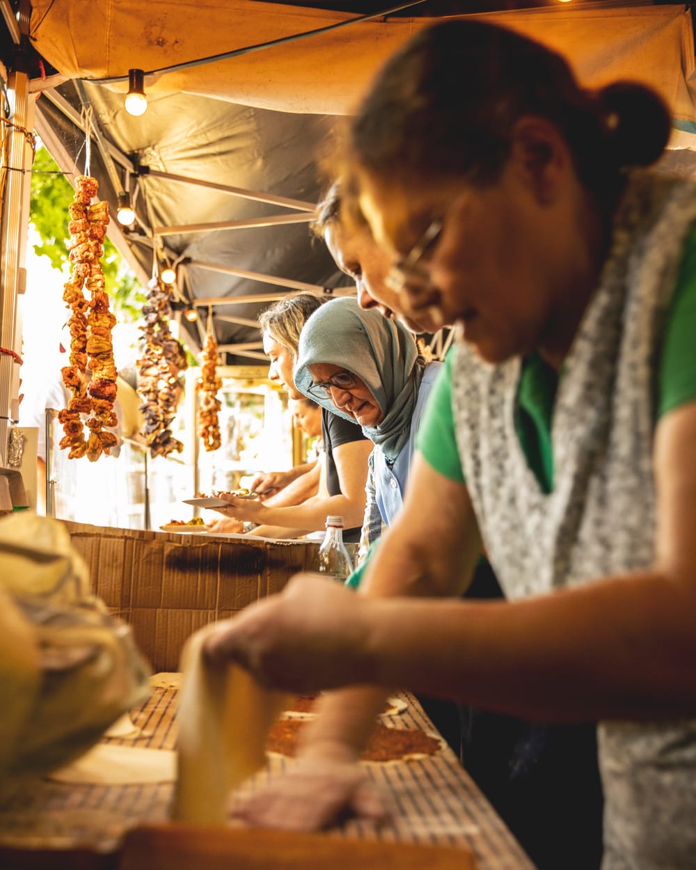 Die Familie beim Kochen am Stand: Teig wird ausgerollt, im Hintergrund Spieße über der Glut