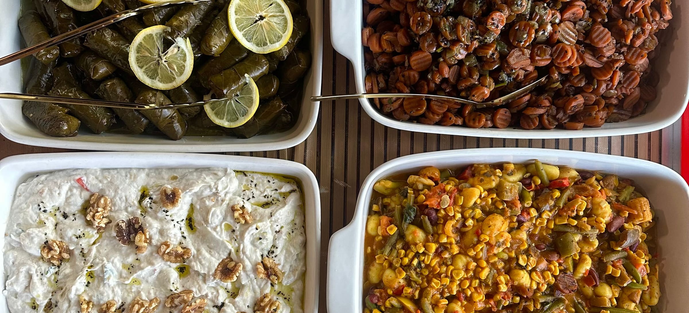 Acht weiße Schalen mit Mezze von oben: gefüllte Weinblätter, Bohnen, Haydari mit Walnüssen, Gemüsepfanne, scharfe Paste